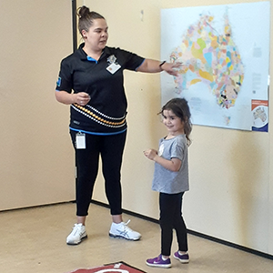 A young Aboriginal woman is pointing to a map of Australia with Aboriginal countries marked, a young Aboriginal girl is standing nearby looking happy and proud.